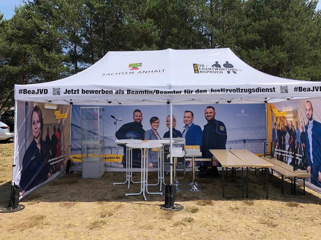 Justizvollzug Sachsen-Anhalt: Recruiting-Kampagne 5 Infostand der Justizvollzugs-Kampagne im Messezelt mit Kampagnenmotiven und Stehtischen – Werbefotografie